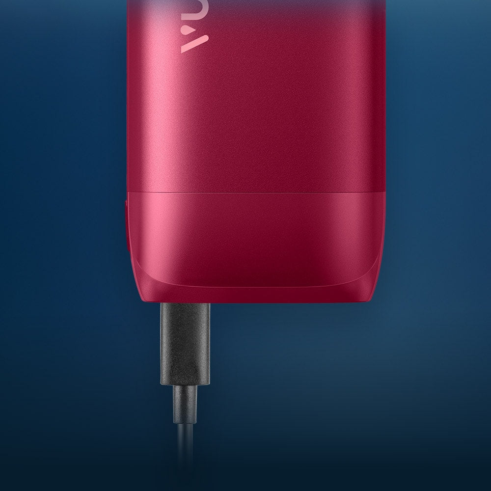 Vuse Ireland A close-up of a red electronic device with a black charging cable plugged into the bottom against a blue background.